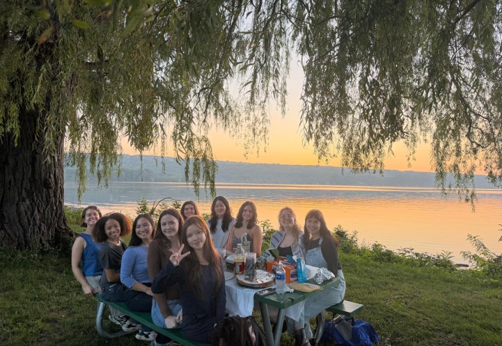 PhD students having a picnic next to Cayuga Lake, beneath a willow tree, with golden hour light