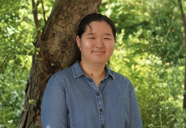 A woman stands in front of a tree smiling.
