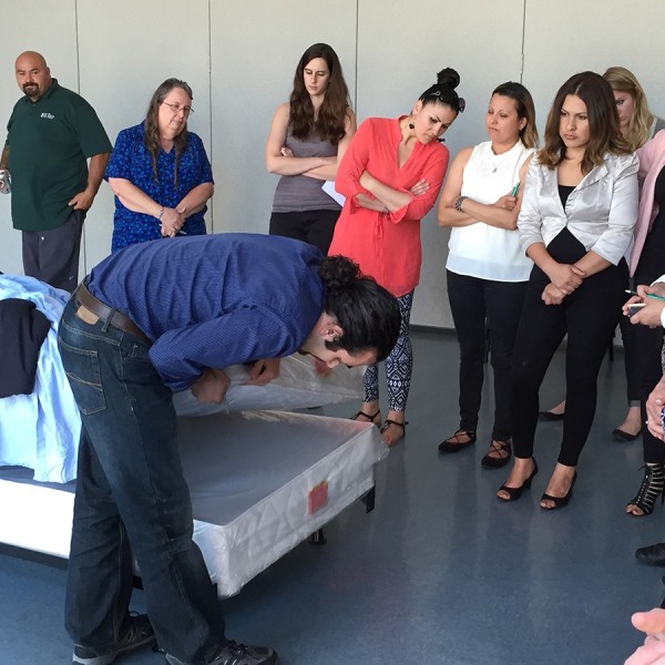 Man checks mattress for bed bugs in front of group