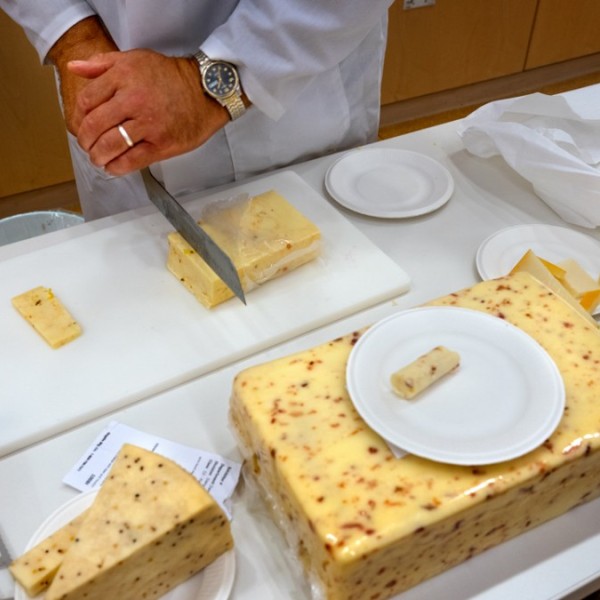 A taster cuts off a slice of cheese to taste.