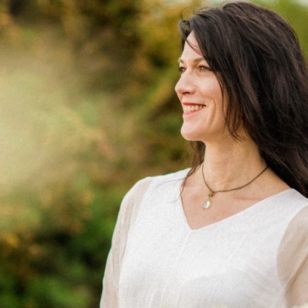 The side profile of a woman wearing a white shirt and smiling with a garden behind her