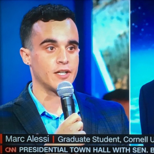 A split screen of a male student holding a microphone asking a question of a male presidential candidate 