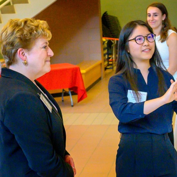 A female student standing in front of a poster and explaining it to an older female who is stanidng be