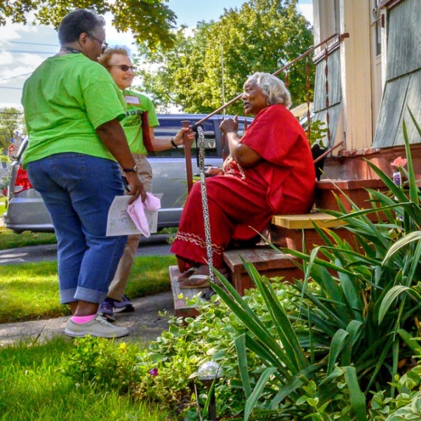 A black older woman sitting on her front stairs in front of her garden