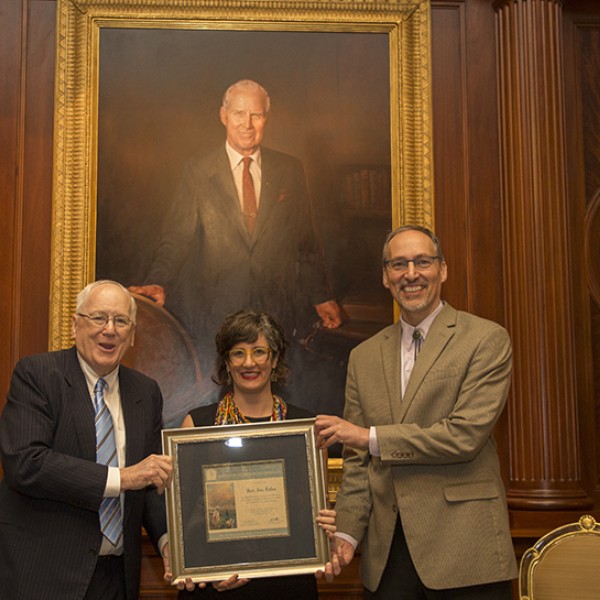 A female holding a framed award between two suited men 