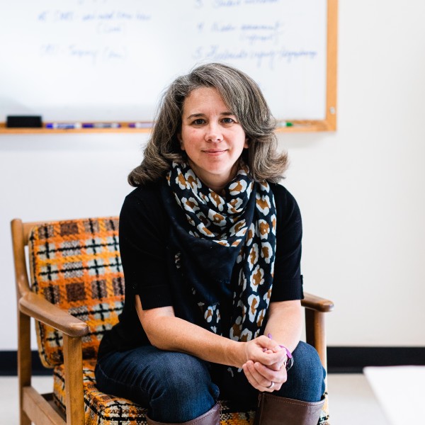 A caucasian female sitting in a chair in an office with a white board behind her