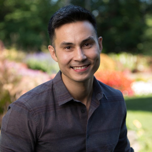 An asian male sitting in a garden smiling at the camera