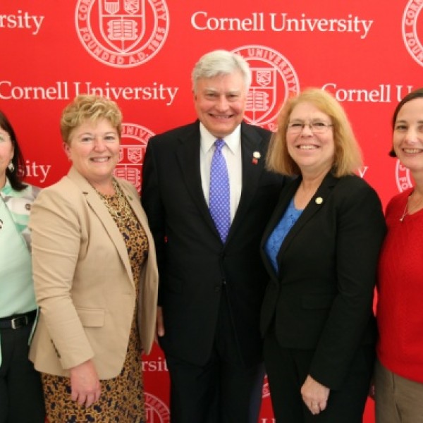 Four women and a man pose together for a photo in front of the Cornell seal