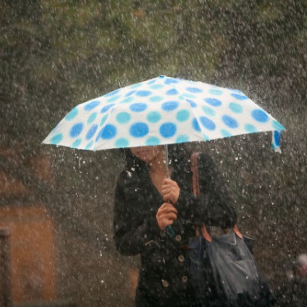 A woman walks in the pouring rain under a blue and white polka-dot umbrella