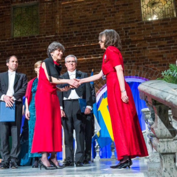 A woman shakes hands with another woman on stage at a recognition ceremony