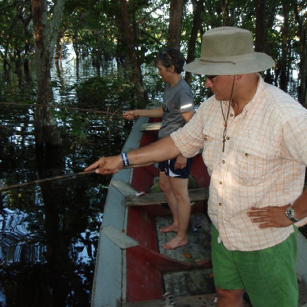A man and a woman stand in a boat on a river with fishing rods in the water