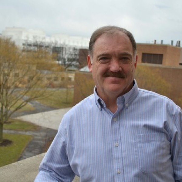 A man stands outside with Cornell campus buildings in the distance