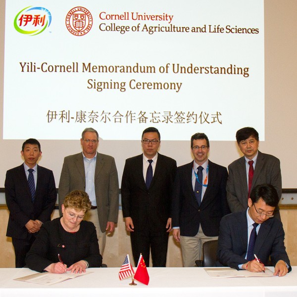 A woman and a man each sign documents as five men stand behind them in a row
