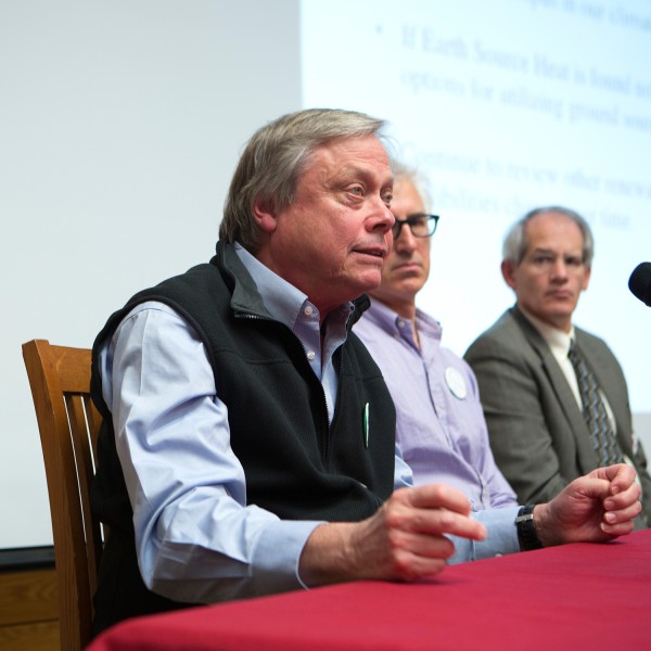 Three men sitting at a table speaking into microphones 