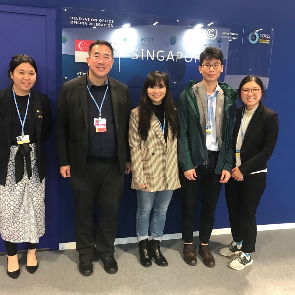 Four college students and one man stand in front of a sign for the delegation of Singapore
