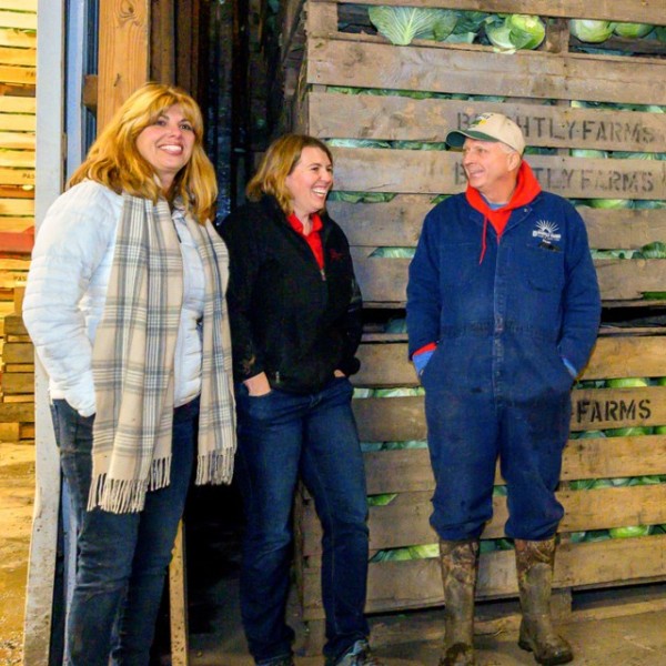 Two women and one man standing in front of crates of cabbage