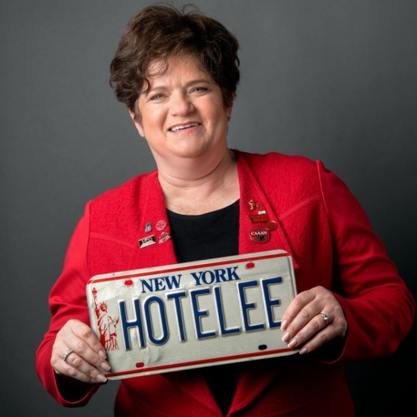 A woman in Cornell jacket presents a license plate that reads "HOTELEE"