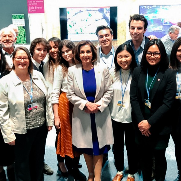 A group of male and female students standing and smiling with an older woman standing in the center of them