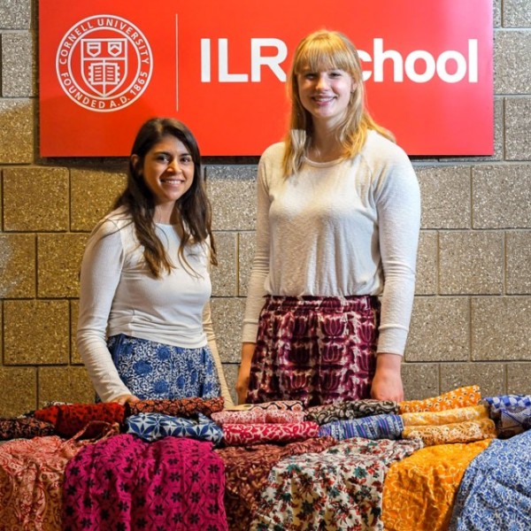 Two female students standing behind a table of colorful pants