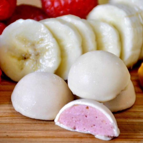 raspberries, a spoonful of peanut butter, sliced bananas and white smoothie bites on a wooden surface