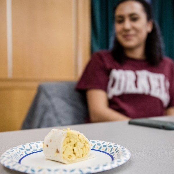 A student sitting at a table with an egg burrito on a paper plate