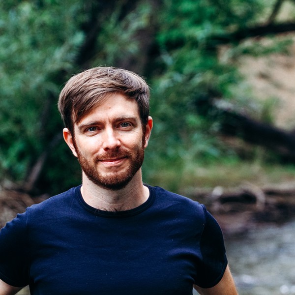 Flavio Lehner standing outside in front of water and green trees 