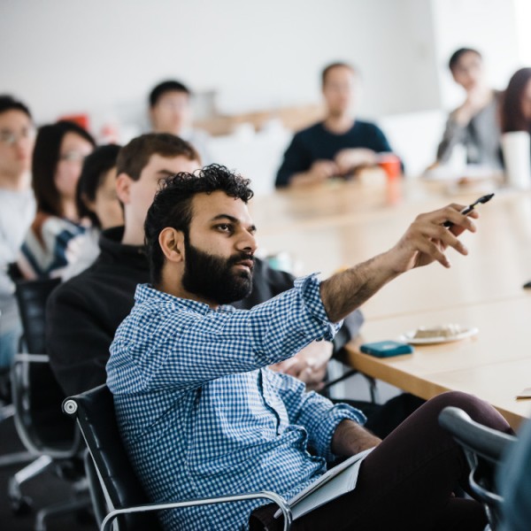 A man sitting at a table and gesturing at something out of frame. Other people are sitting at the table with him