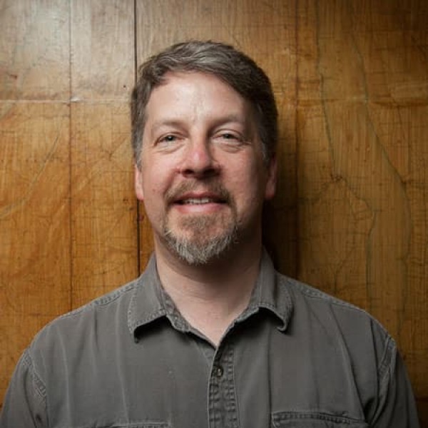 A headshot of a man in front of a wooden wall