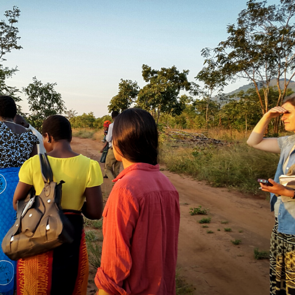 A group of people walk on a road beside a field