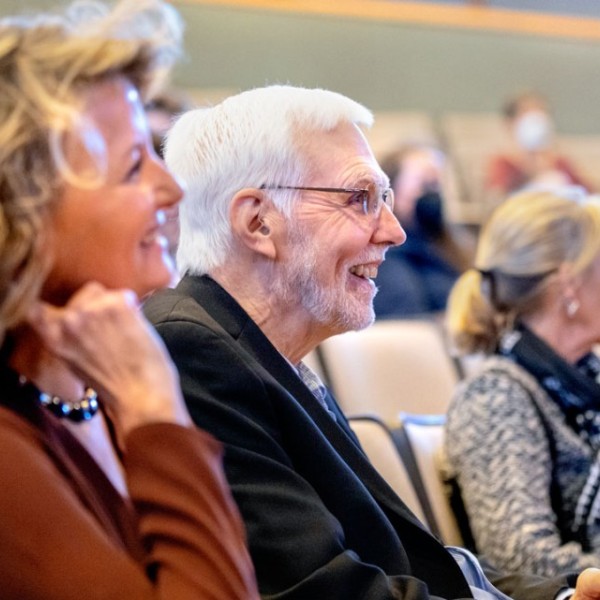Julia Thom-Levy and Peter Lepage sitting in auditorium chairs smiling.