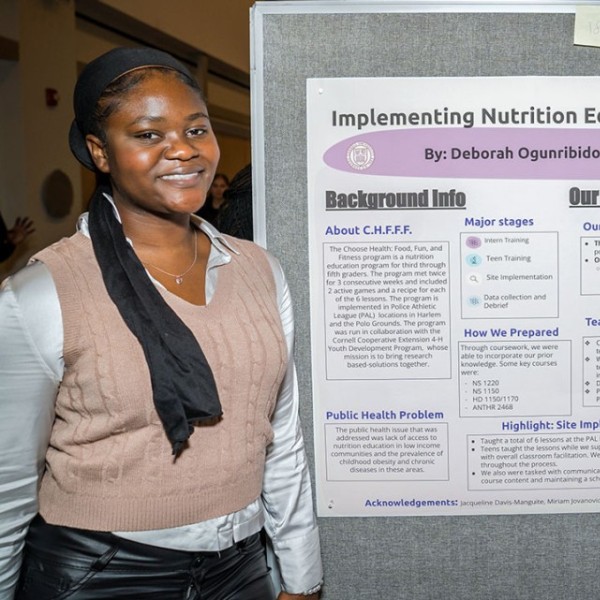 Two students stand beside their project poster which reads "Implementing Nutrition Education in Harlem, NY."