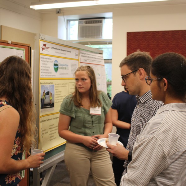 A group of interns grouped around a research poster that is being presented by Megan Guy, who is standing on the left.