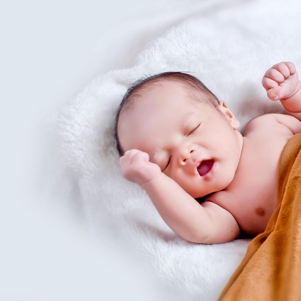 A baby lays on a white rug with a gold blanket on top of it.