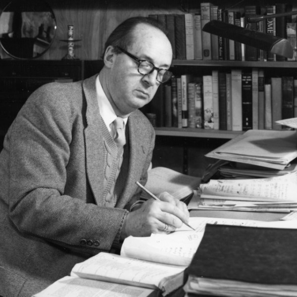 A black and white photo of a man sitting at a desk and writing into a journal.