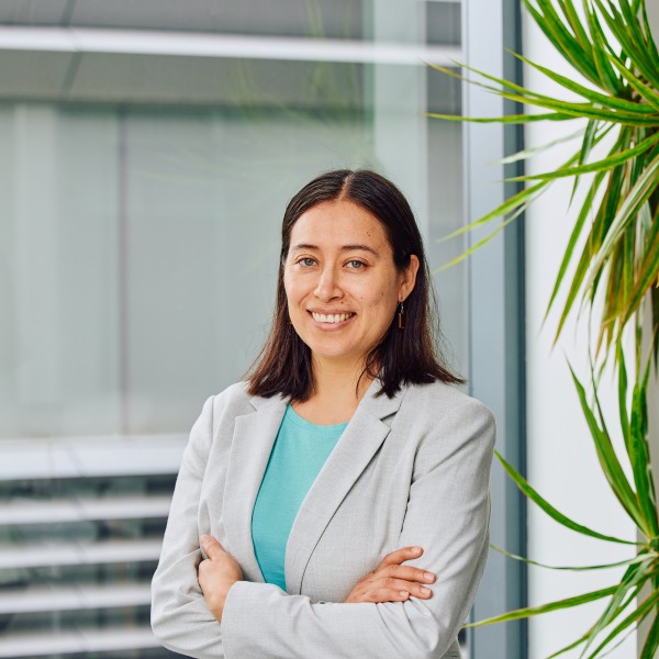 Person in a turquoise shirt and grey blazer standing in front of a window 