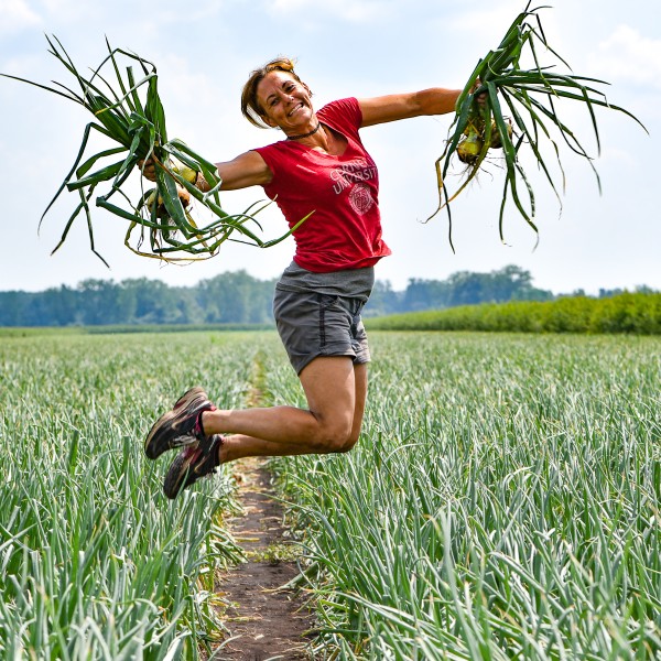 Christy Hoepting jumping in a field of onions, with onions in her hands