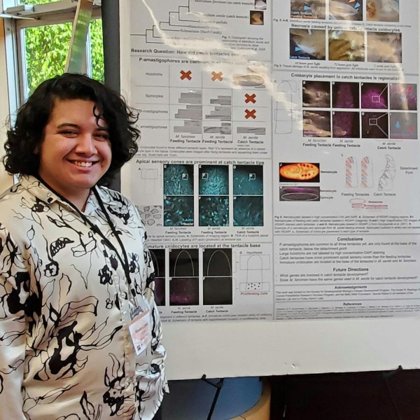 Students stands next to poster presentation.