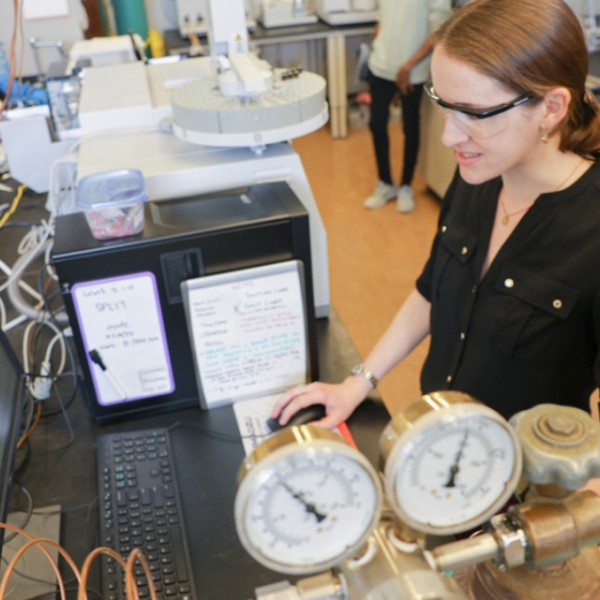 Two researchers wearing safety goggles look at something on a computer