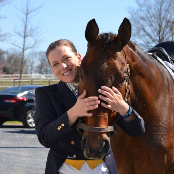 A headshot photo of Erika Machtinger smiling and standing with a brown horse