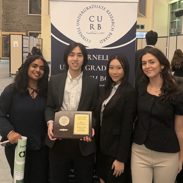 four students stand holding a plaque saying "peoples choice" in front of their poster