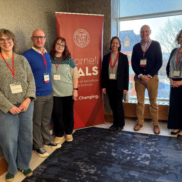 6 individuals stand in front of Cornell CALS poster