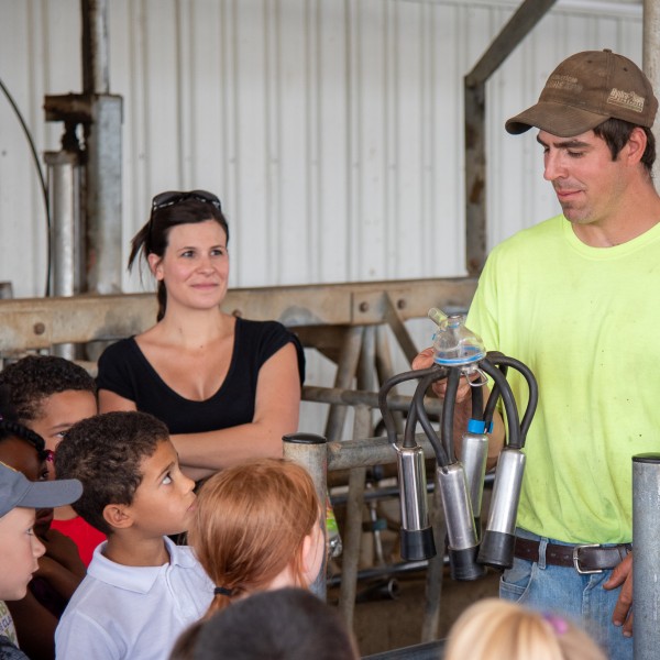 Cheryl on a farm tour with schoolkids. A farmer holds a miling machine in his hand, showing it to the kids.