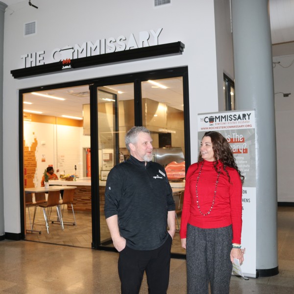 A man and a woman standing together in front of a room with a sign that reads "The Commissary"