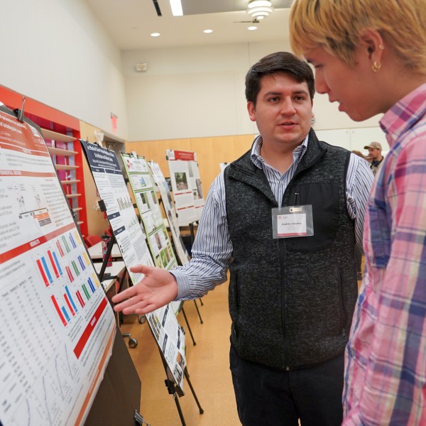 a man gestures at an academic poster while another man watches