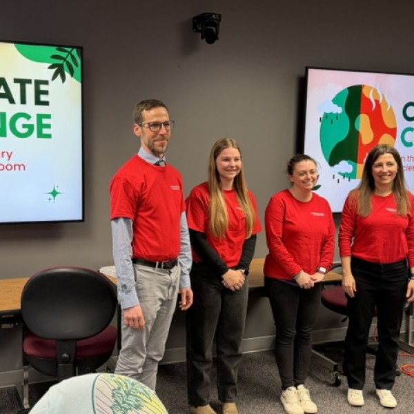Four individuals in red t-shirts stand in a classroom next to screens displaying "CLIMATE CHANGE."