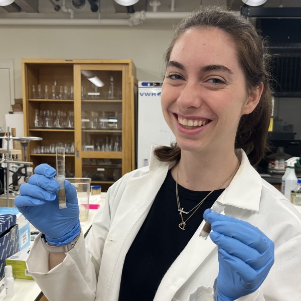 A woman holds two test tubes and smiles.
