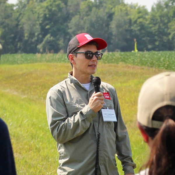 Louis Longchamps speaking to a group of people at a farm