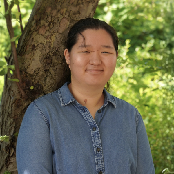 A woman stands in front of a tree smiling.