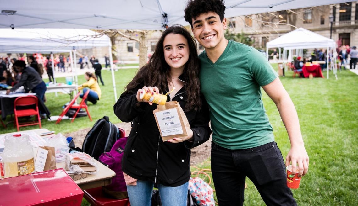 A male and female student standing under a tent holding popcorn and smiling