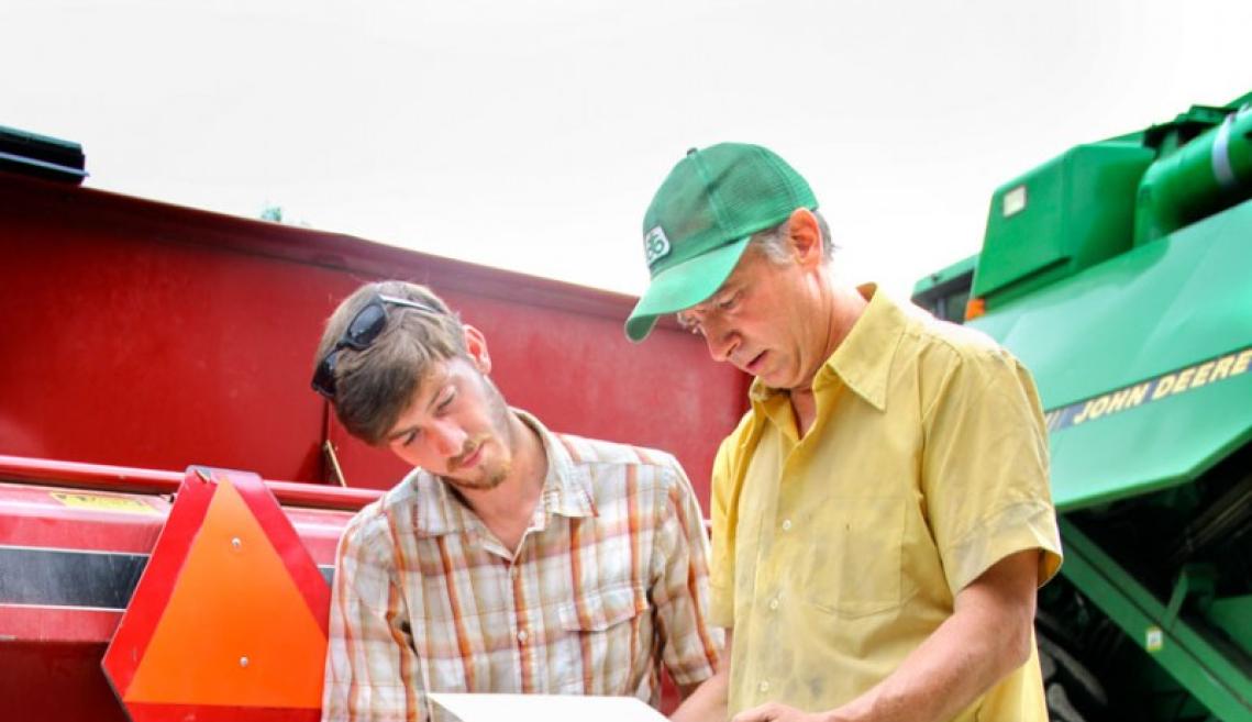 2 men sitting on factory equipment flip through papers